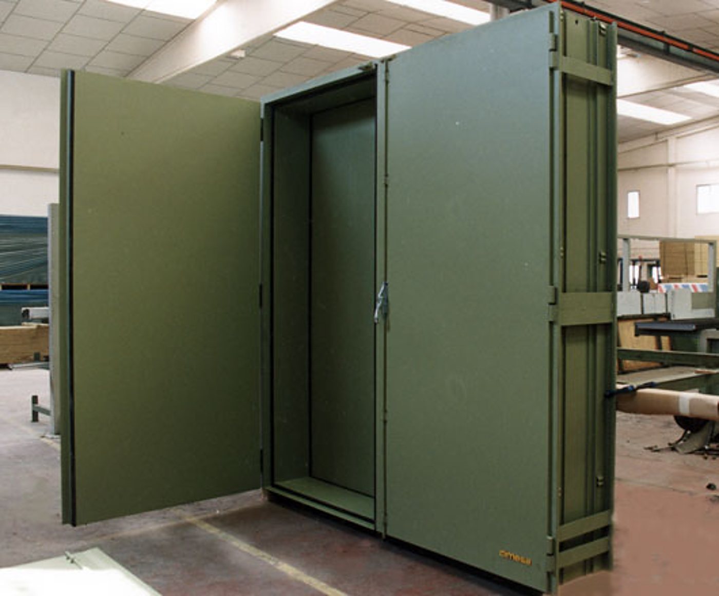 Une grande armoire métallique de couleur vert kaki, dont les deux portes sont ouvertes, est installée dans un atelier industriel.